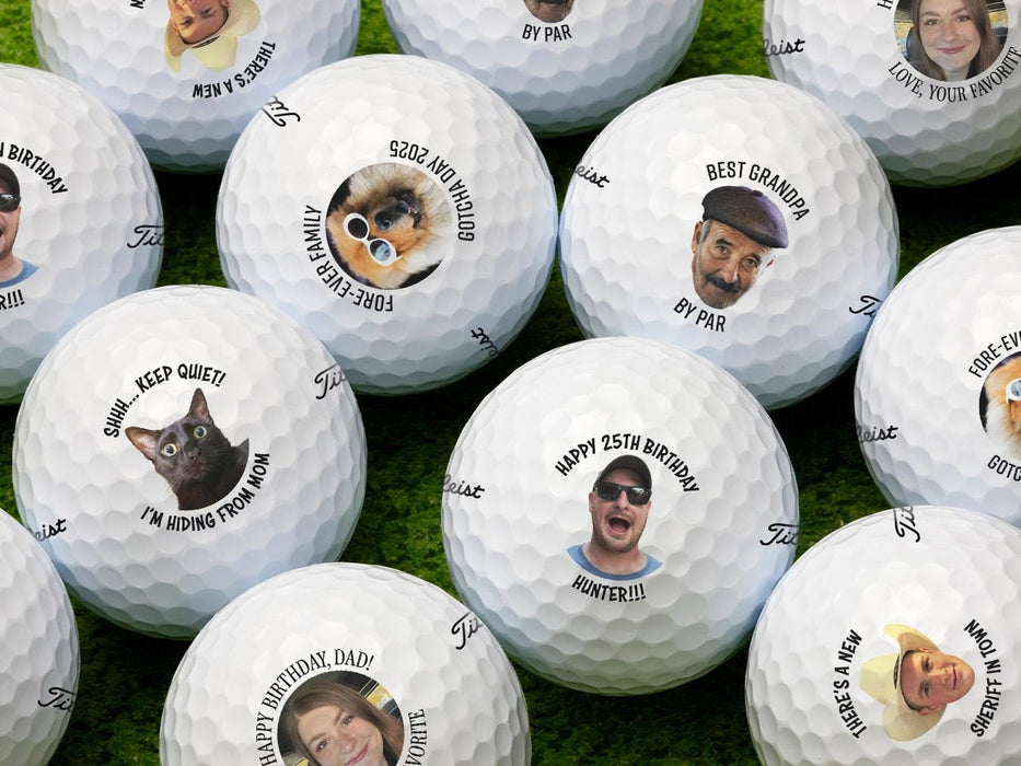 Multiple Titleist golf balls shown with different photos and text on each ball. Golf balls sit on a grassy surface.