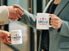 two business people shaking hands and holding white mugs with red white and blue American designs with typography that says Amelia and Timothy for America with Red Stars