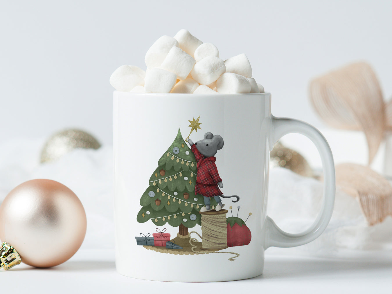 white mug with mouse decorating christmas tree artwork surrounded by pink and gold ornaments, and pink bows and white boxes on a white table