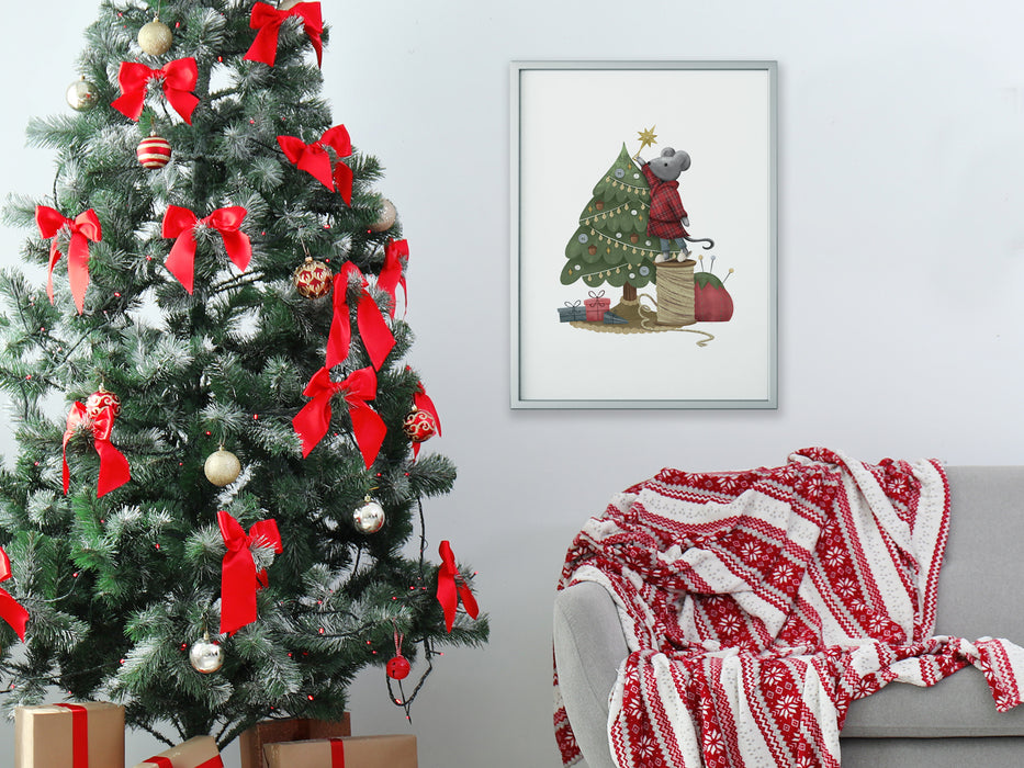 silver frame hanging on white wall with a christmas print of mouse decorating tree surrounded by holiday decor such as a christmas tree with bows and ornaments, christmas gifts, and a grey couch with a red and white blanket