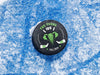 Hockey puck on ice rink with a green elephant animal mascot design with the wordsThe Tusks, 16U, Fall 2024