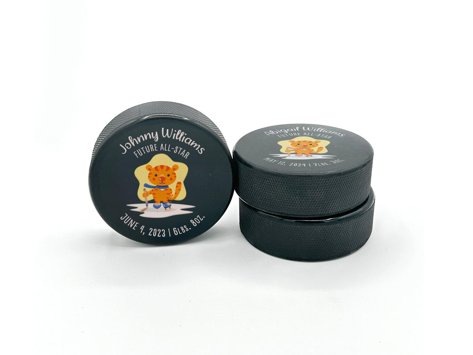 two hockey pucks stacked with future all star cartoon tiger designs with different names, birthdays, weights, blue and pink color options on a white background