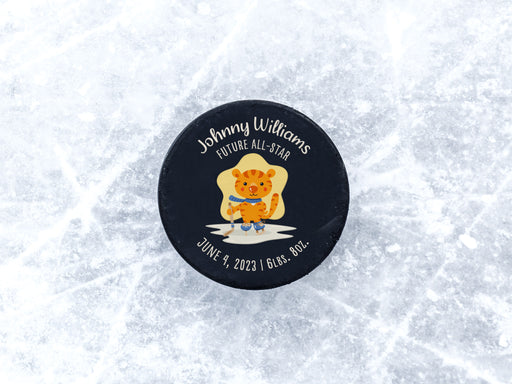 hockey puck ontop of ice with blue future all star cartoon tiger design with the name Johnny Williams on it with birthday and weight