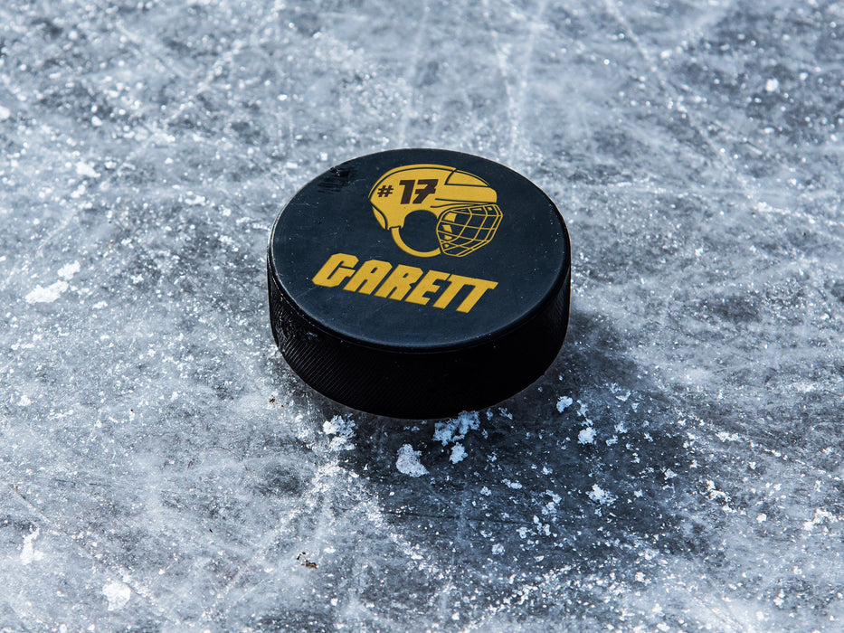 single hockey puck on ice rink with helmet design printed in yellow that says Garett number 17