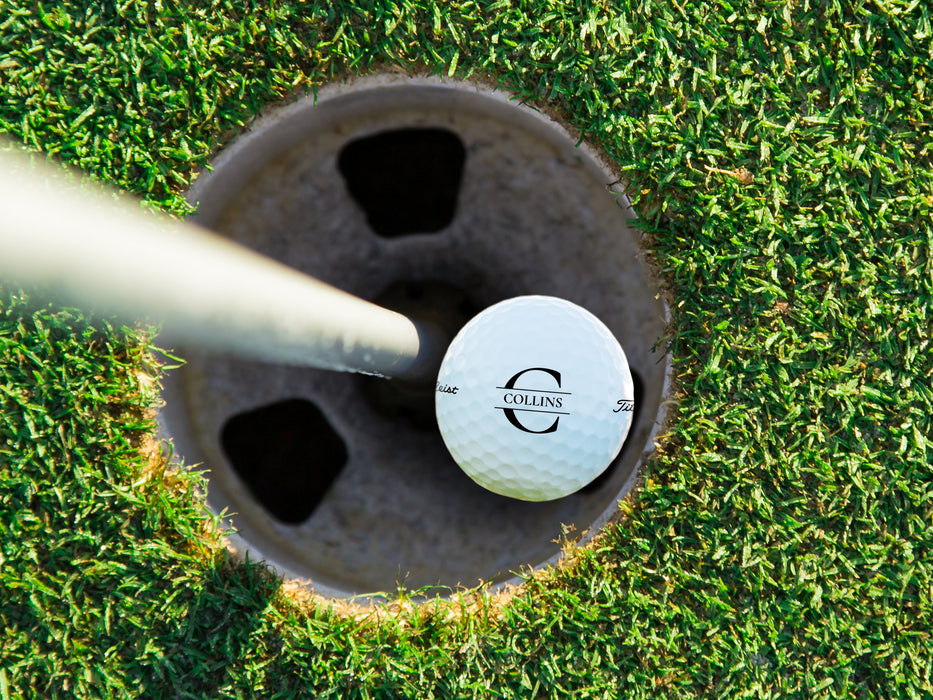 single white titleist golf ball with custom personalized black initial printed design in golf course hole next to pole surrounded by grass golf course background