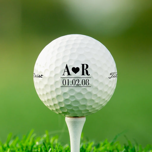 single white titleist golf ball with customizable personalized initials and heart design on white golf tee on golf course grass background