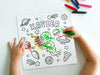 kid at white table coloring a canvas panel with a custom space alien adventure design printed on it using crayons with a pile of crayons right next to the canvas