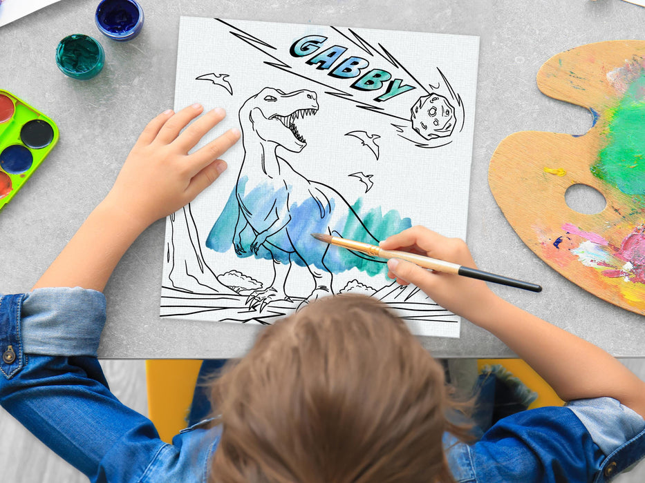 kid painting a canvas panel with a custom name dinosaur t-rex design printed on it, kid is using watercolors on grey table surrounded by painting supplies such as cups of paint, palettes, brushes, etc