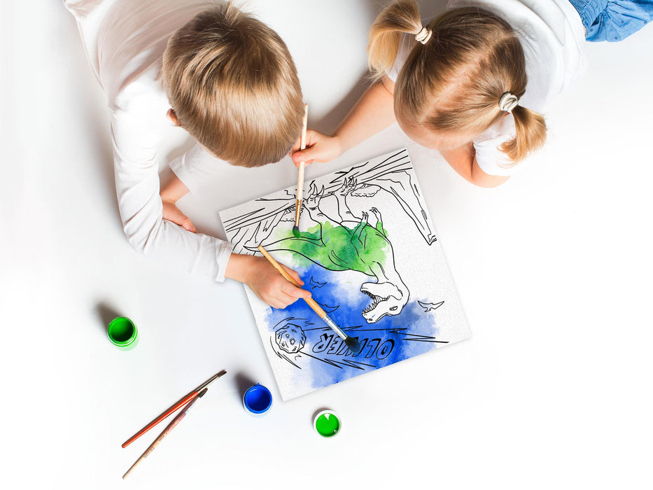 two kids on white floor painting a a custom caticorn design printed on it with green and blue paint as well as paint brushes