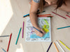 kid sitting on the wooden floor coloring a canvas panel with a custom space alien adventure design printed on it using colored pencils