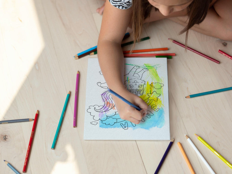 kid sitting on the wooden floor coloring a canvas panel with a custom name caticorn design printed on it using colored pencils