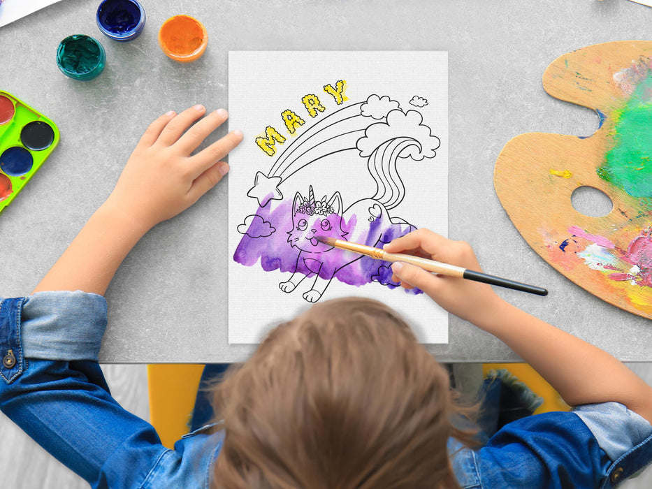 kid painting a canvas panel with a custom name caticorn design printed on it, kid is using watercolors on grey table surrounded by painting supplies such as cups of paint, palettes, brushes, etc