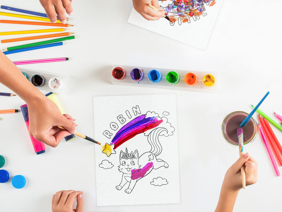 two kids and an adult painting two canvas boards with custom caticorn printed on it with custom names, placed on white table surrounded by art supplies such as paint, markers, pens, highlighters, etc