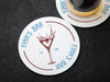 One coaster has a beer glass on it and an empty coaster sits beside it. Coasters feature bar design. This design uses blue lettering and a drawing of a martini glass. The name, established date, and location can be customized.