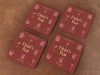 Four coasters sit on a leather background. Coasters feature bar design. This design uses yellow lettering on a red background with drawings of drink glasses. The name, established date, and location can be customized.