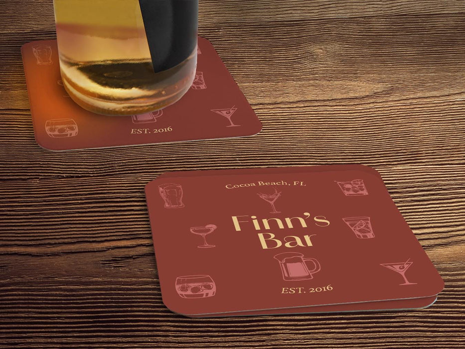 One coaster has a beer glass on it and an empty coaster sits beside it. Coasters feature bar design. This design uses yellow lettering on a red background with drawings of drink glasses. The name, established date, and location can be customized.