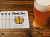 A stack of coasters are spread out across a dark wood surface next to a beer glass. Coasters feature bar design. This design uses brown and orange lettering, and a drawing of beer glasses. The name, established date, and location can be customized.