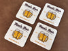 Four coasters sit on a leather background. Coasters feature bar design. This design uses brown and orange lettering, and a drawing of beer glasses. The name, established date, and location can be customized.