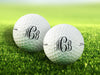 two white titleist golf balls with custom personalized black scroll monogram printed designs on grass golf course in the background