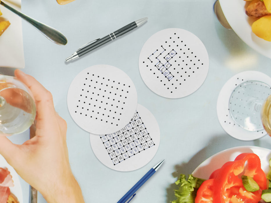 three white coasters with dots and boxes party game design on blue dinner table surrounded by thanksgiving food as well as a hand grabbing a wine glass