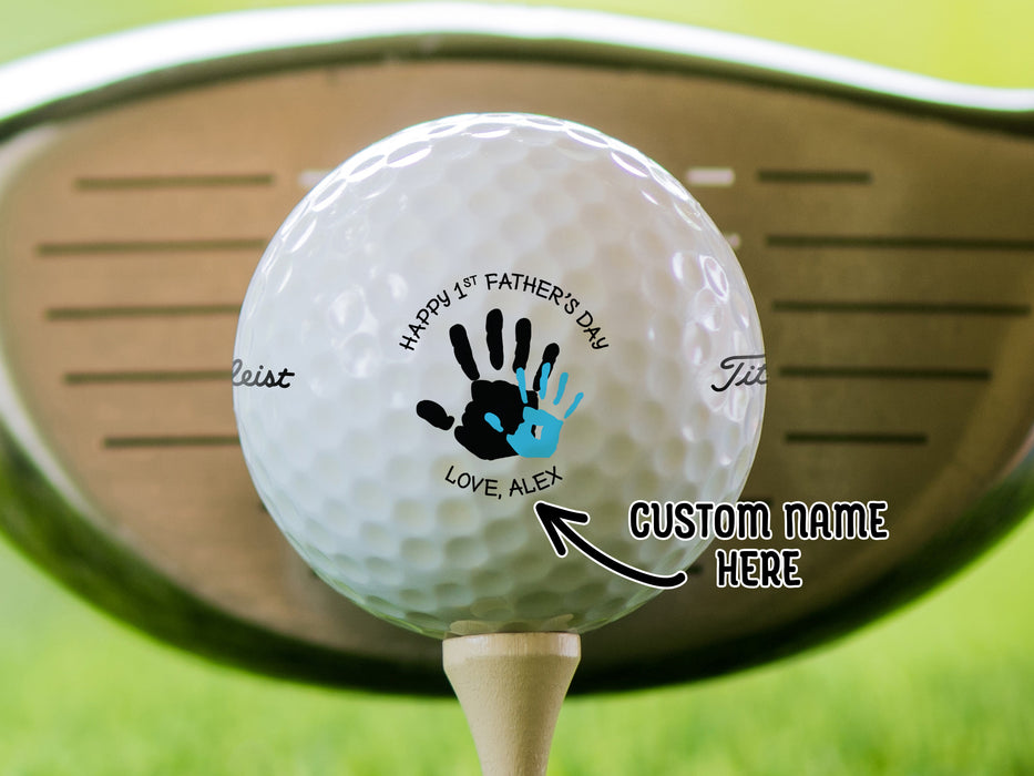 single white titleist golf ball with custom personalized name happy 1st fathers day handprint design on beige golf tee with golf club and golf course grass in the background