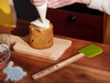 person icing a cake on wooden table next to green colored spatula with wooden handle engraving that says Fatimas Bakery with Cupcake 2 icon