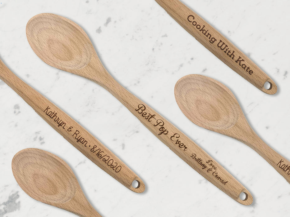 multiple different wooden spoons across marble table with different engravings on the handles such as names, dates, and messages