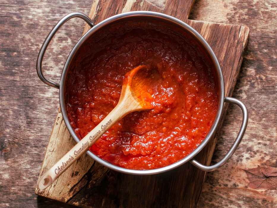 wooden spoon in a pot full of sauce ontop of wooden table with engraving on the handle that says Chelseas Sunday Sauce Spoon