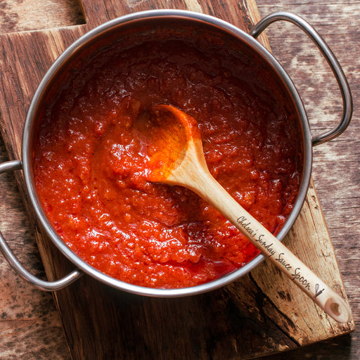 wooden spoon in a pot full of sauce on top of wooden table with engraving on the handle that says Chelseas Sunday Sauce Spoon with the whisk and pin icon.