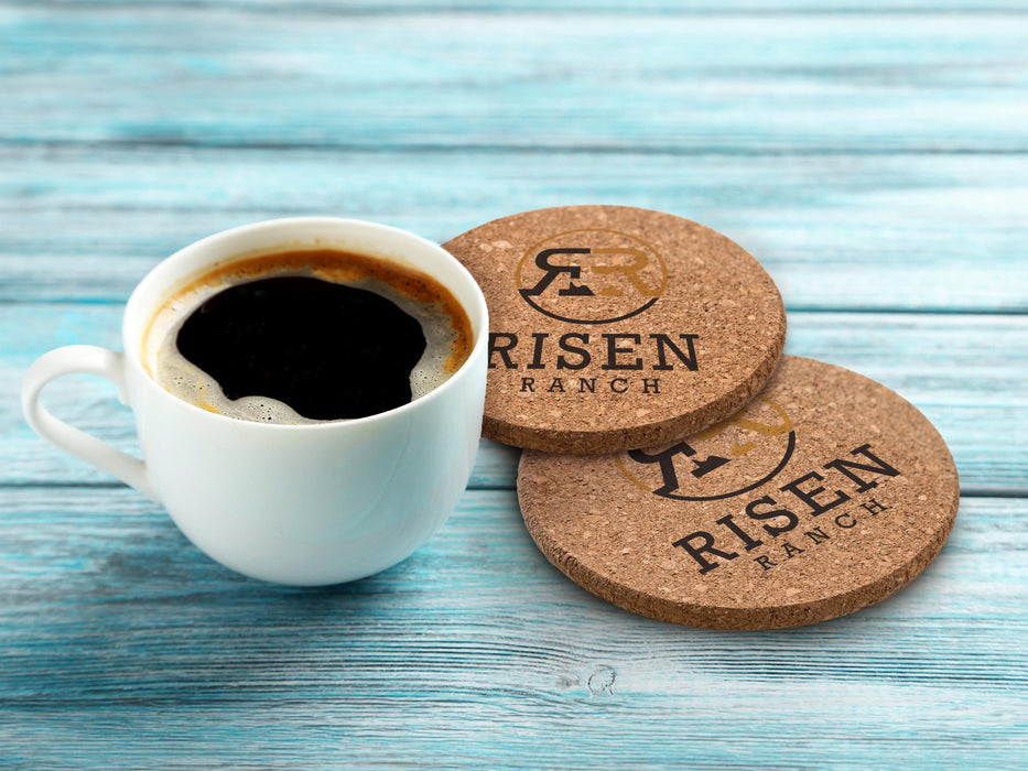 Two coasters sit on a blue wooden surface with a coffee cup on the side.