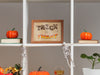 Single wooden frame with halloween typography print on decorated shelves with halloween decor such as pumpkins, skeletons, and plants