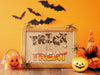 single wooden frame with halloween trick or treat typography print against orange wall surrounded by spider, jack o lanterns, witch hat decor