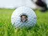 Titleist golf ball is shown on a grassy golf course. Ball features custom text and photo design.