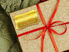 A gold foil cardstock gift tag is shown on a glitter wrapped box. The box also has a red ribbon on it. The box is seen on a green blanket surface.