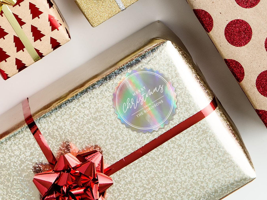 A rainbow cardstock gift tag is shown on a Christmas present. The present is wrapped in gold paper and has a red bow and ribbon around it. The background of the picture is a white surface.