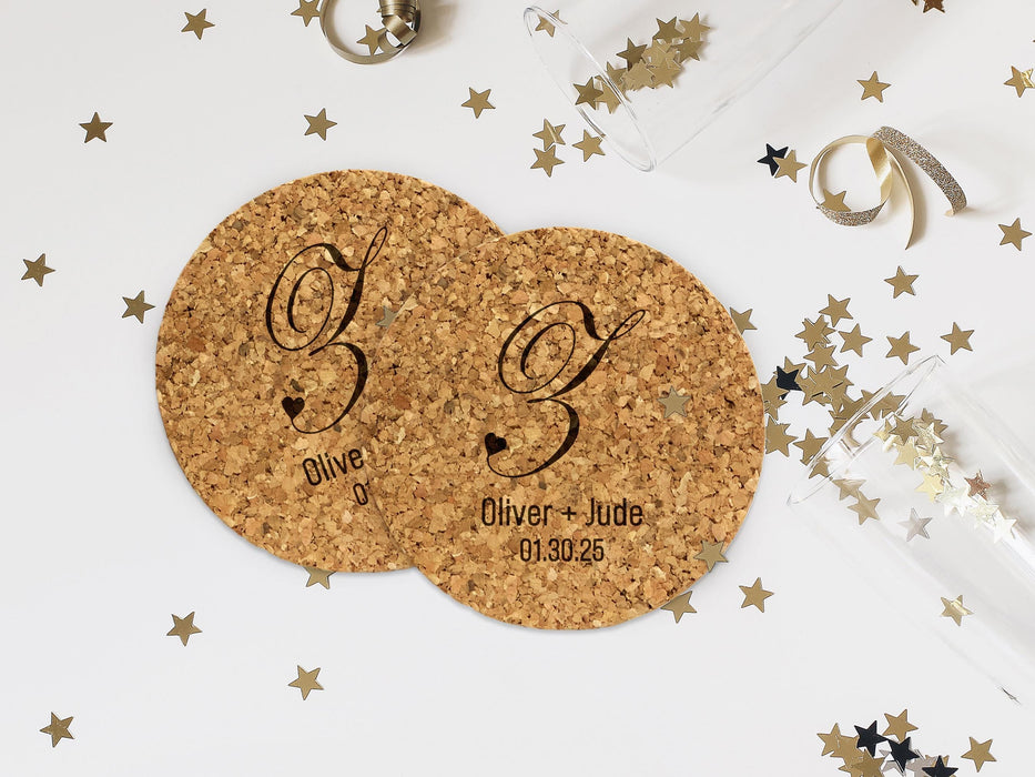 Two coasters lay on white surface with champagne glasses and gold stars surrounding them. Coasters feature heart initial design with a monogram, couples names, and wedding date.