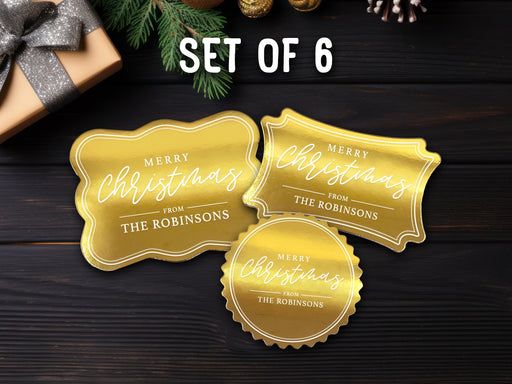 Text reads, Set of 6. Three gold foil cardstock Merry Christmas gift tags are shown on a dark wooden surface. Pine tree branches and a Christmas present are shown around the tags.