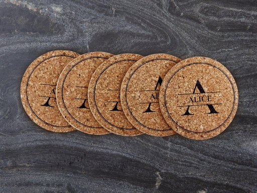 A stack of monogram coasters are spread out on a marble surface. The coasters display the name Alice with a lined circle frame around it.