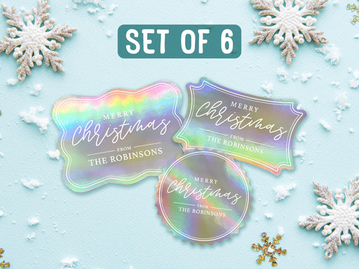 Text reads, Set of 6. Three iridescent foil cardstock Merry Christmas gift tags are shown on a light blue surface surrounded by snowflakes.