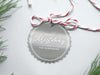 A silver foil cardstock Merry Christmas gift tag is shown sitting on a white background surrounded by Christmas tree clippings. The tag has a red and white string looped through the top of it.