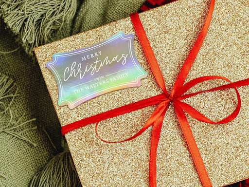 A rainbow cardstock gift tag is shown on a glitter wrapped box. The box also has a red ribbon on it. The box is seen on a green blanket surface.