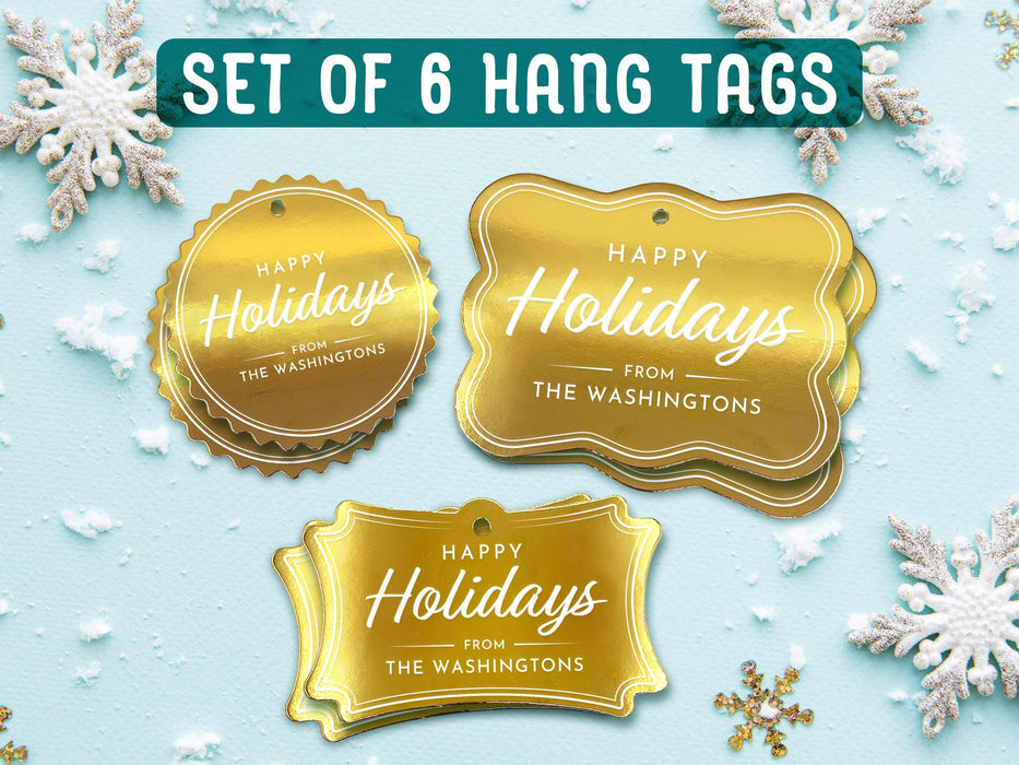 Text reads, Set of 6 Hang Tags. Six gold foil cardstock Happy Holidays gift tags are shown on a light blue surface surrounded by snowflakes.