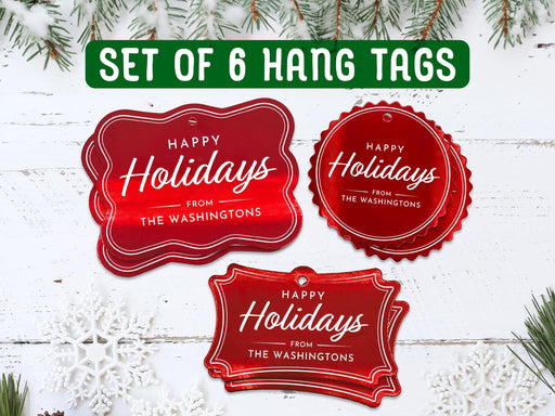 Text reads, Set of 6 Hang Tags. Six red foil cardstock Happy Holidays hang tags are shown on a white wooden surface. Pine tree branches and snowflakes surround the tags.