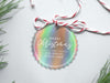 An iridescent cardstock Merry Christmas gift tag is shown sitting on a white background surrounded by Christmas tree clippings. The tag has a red and white string looped through the top of it.