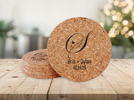 A stack of coasters sit on a wooden surface, with a single coaster standing upright. Coasters feature heart initial design with monograms, couples names, and wedding date.