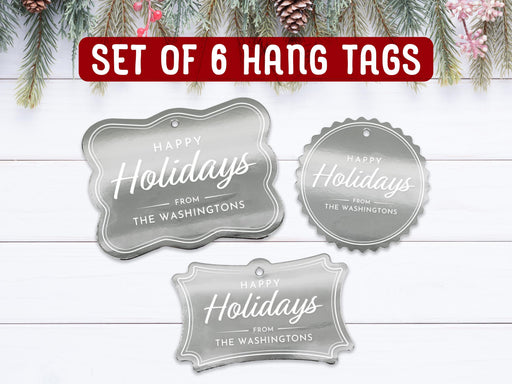 Text reads, Set of 6 Hang Tags. Six silver foil cardstock Merry Christmas hang tags are shown on a white wooden surface. Pine tree branches and holly berries are shown above the tags.