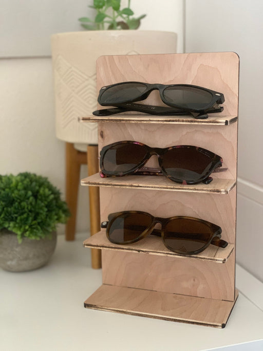 wooden glasses stand with multiple sunglasses sitting on a countertop surrounded by multiple potted plants