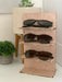 wooden glasses stand with multiple sunglasses sitting on a countertop surrounded by multiple potted plants