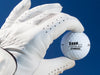 White gloved hand holding single white Titleist golf ball with Shhh I'm Hiding From design in front of dark blue background