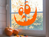 orange goofy pumpkin face on indoor window next to pumpkins and fall leaves